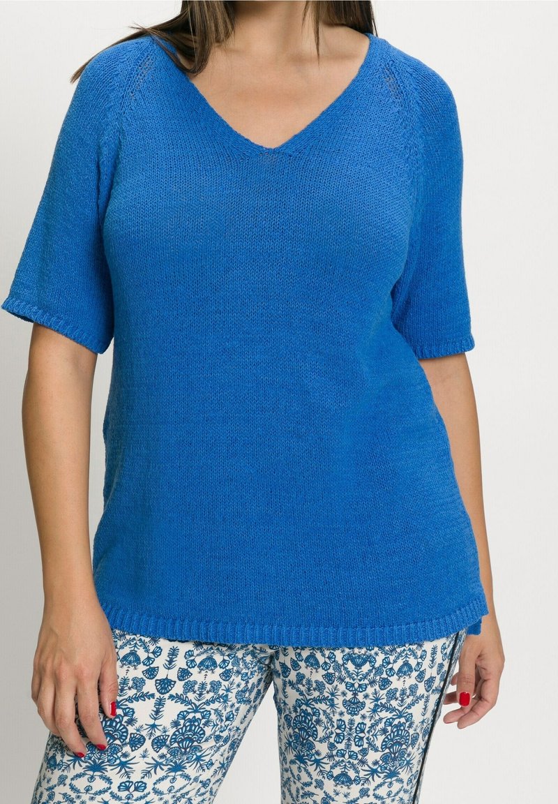 Modrý krátký rukáv svetr s výstřihem do V, s hladkým povrchem. V kombinaci s vzorovanými kalhotami s modro-bílými květinovými motivy.