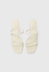 White strappy sandals with a rectangular toe shape, smooth texture, and thin straps, featuring a minimalistic design and slight heel.