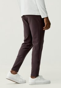 Mörklila joggingsbyxor med slim fit, utrustade med sid dragkedjor vid anklarna, kombinerade med vita sportskor och en långärmad vit topp.