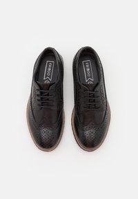 Černé kožené boty s brogue detaily, kulatou špičkou, šněrovacím designem a hnědou gumovou podrážkou. Hladký povrch s jemnými perforacemi.