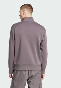 Felpa in pile di lavanda tenue, con colletto alto, polsini e orlo a coste. Indossata con pantaloni cargo grigi abbinati.