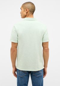 Jasnozielona koszulka polo z krótkim rękawem o strukturalnym wykończeniu i klasycznym kołnierzykiem, w połączeniu z niebieskimi dżinsami.