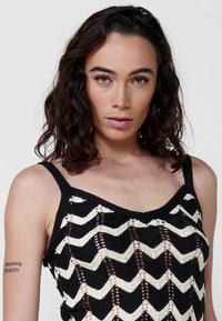 Top lavorato a maglia a motivo chevron bianco e nero con finitura testurizzata, presenta spalline strette e un design semi-trasparente.