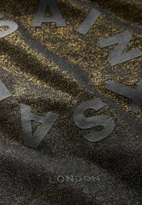 Tejido negro texturizado con brillo dorado, con letras mate negras en relieve que dicen "PAINT" y "LONDRES" en el borde inferior.