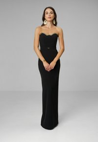 Czarna sukienka bez ramiączek o dopasowanej sylwetce, z falistym złotym wykończeniem wzdłuż dekoltu oraz subtelnym akcentem w talii. Gładka faktura materiału.