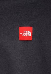 Tessuto nero con una finitura testurizzata presenta un'etichetta quadrata rossa che mostra "THE NORTH FACE" e un logo bianco a mezza cupola.