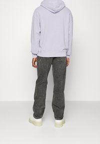 Lilac hoodie with a relaxed fit and large hood, paired with gray denim pants and chunky white-soled shoes. Textured fabric details visible.