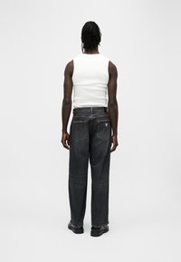 Μαύρο τζιν παντελόνι με φαρδιά πόδια, δύο πίσω τσέπες και αντίθετη ραφή, σε συνδυασμό με λευκό αμάνικο τοπ. Λείο υλικό και άνετη εφαρμογή.