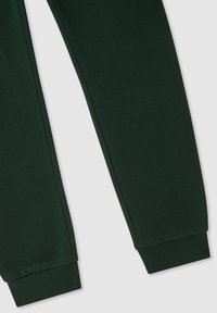 Zielone dresowe spodnie z miękką fakturą, z elastycznymi mankietami i zwężanym krojem. Brak widocznych wzorów lub detali metalowych.