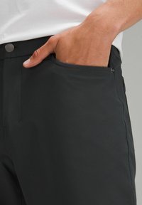 Pantalons noirs en tissu lisse et léger, dotés d'une poche latérale avec fermeture à bouton et d'une taille structurée.