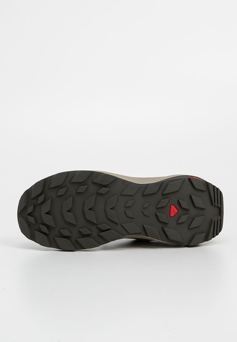 Suela de zapatilla deTrail running con un patrón de goma negra texturizada, que presenta clavos angulares para mayor agarre y un acento rojo cerca del talón.