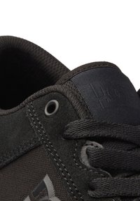 Black sneaker featuring a suede upper, mesh tongue, and textured rubber sole. Includes eyelet and logo detailing in contrasting material.