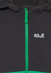 Schwarze Jacke mit grünem Reißverschluss und Akzenten, ausgestattet mit einer mit Fell gefütterten Kapuze und dem weißen "Jack Wolfskin"-Logo auf der Brust.