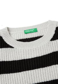Pletený svetr s kulatým výstřihem; má střídající se černé a bílé pruhy; obsahuje zelenou nálepku s nápisem "UNITED COLORS OF BENETTON."