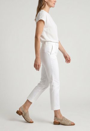 Kobieta chodząca ubrana w całkowicie biały strój, z beżowymi plecionymi sandałami typu slingback z odkrytymi palcami, na jasnym tle.