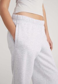 Pantaloni della tuta grigio chiaro realizzati in tessuto morbido, dotati di una vita elasticizzata, tasche laterali e una vestibilità comoda con una consistenza liscia.