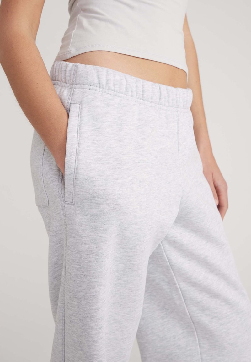 Pantaloni della tuta grigio chiaro realizzati in tessuto morbido, dotati di una vita elasticizzata, tasche laterali e una vestibilità comoda con una consistenza liscia.