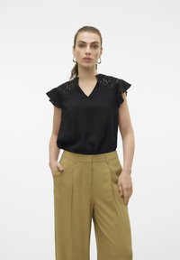 Top nero a maniche corte con scollo a V e dettagli in pizzo sulle spalle, abbinato a pantaloni beige a vita alta e gamba larga.