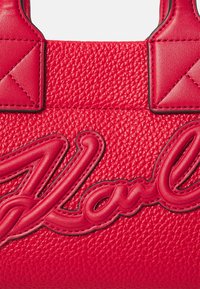 Geantă de mână din piele roșie cu un finisaj texturat, având logo-ul pronunțat "Karl" într-o nuanță roșie asortată și accente ale mânerului unghiular.