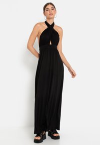 Melna halter maxi kleita ar atslēgas caurumu, savilktu jostasvietu un plūstošu svārku. Stilizēta ar masīviem platformas sandāliem. Gluda, viegla auduma.