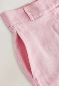 Kõrge vöökohaga roosad püksid kalasaba mustriga, küljetasku ja vööaasaga heledal taustal.