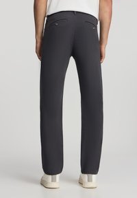 Ciemnoszare spodnie wykonane z gładkiego materiału, z tylnymi kieszeniami ozdobionymi małymi metalowymi guzikami oraz prostym krojem nogawki. Noszone z białymi trampkami.