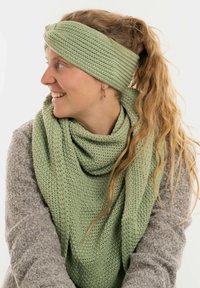 Fascia verde in maglia e sciarpa realizzate in tessuto texturizzato, disposte in modo informale, abbinate a un maglione grigio chiaro.