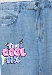 Jeans in denim azzurro chiaro con una texture liscia. Presentano una grande grafica colorata con la scritta "THE COOL ONE" in rosa e viola con accenti decorativi.