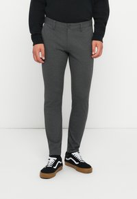 Pantalones ajustados grises hechos de una tela texturizada, con cierre de botón, trabillas para cinturón y bolsillos laterales, combinados con zapatillas negras.