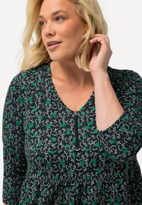 Vestido negro con patrón floral verde, con cremallera en el cuello y mangas tres cuartos. Tejido ligero y texturizado con un diseño acampanado.