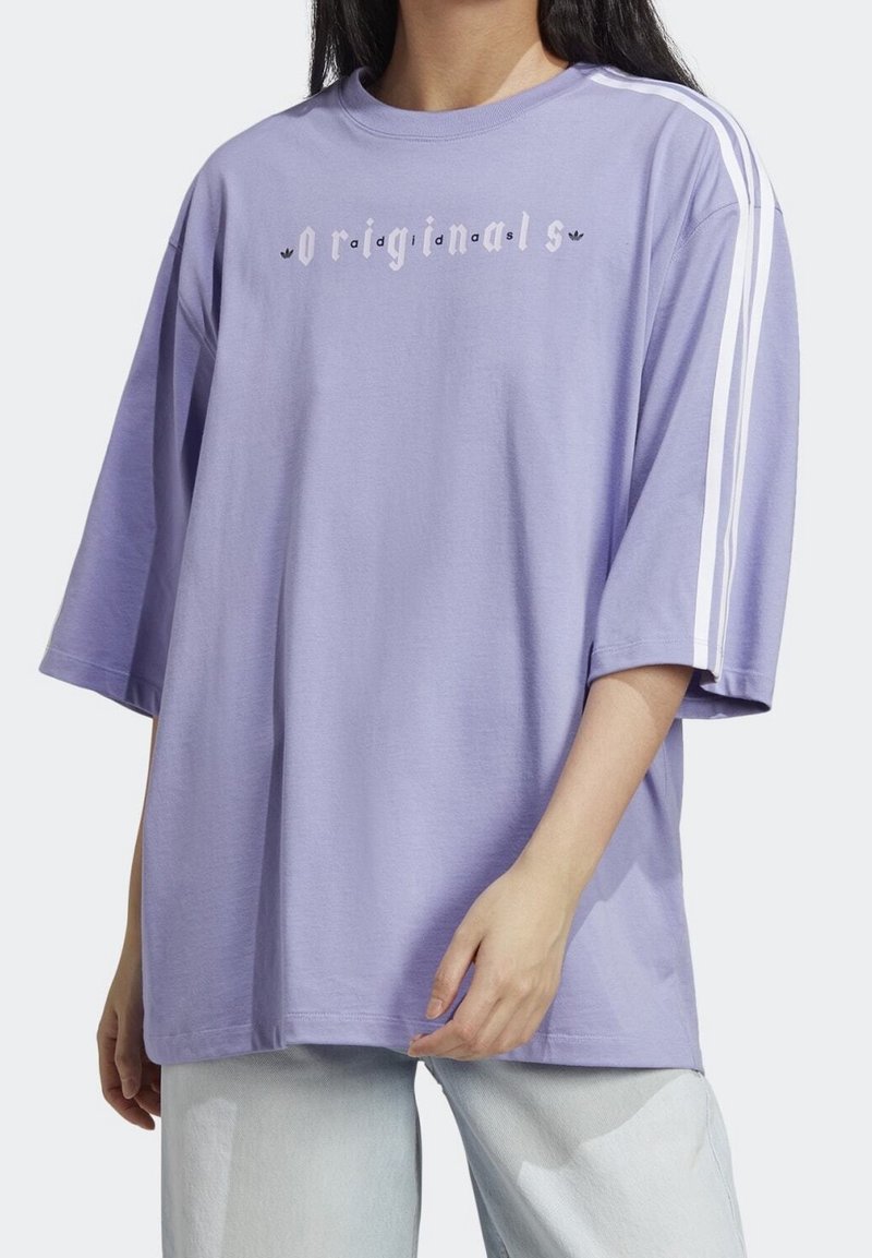T-shirt oversize lavande à manches courtes, accents à trois bandes blanches sur les épaules et logo "originals" imprimé sur la poitrine.