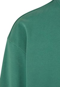 Sweat-shirt en coton vert avec une texture lisse, présentant un design simple et un col arrondi. Le tissu affiche un motif de tricotage subtil et uniforme.