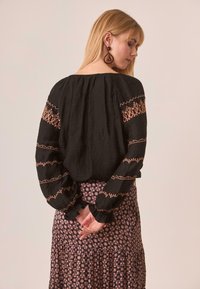 Blusa negra con acentos bordados en óxido, de mangas largas y holgadas. Combinada con una falda de patrón floral en tonos rosas y oscuros.