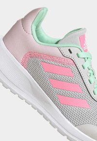 Sneaker grigio con tomaia in rete, dettagli rosa, fodera verde menta e tre strisce rosa laterali. Presenta una suola bianca e lacci.