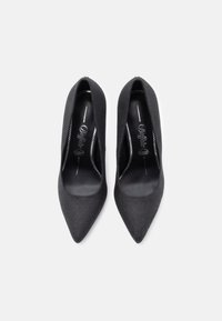 Fekete, hegyes orrú, magas sarkú cipő puha anyagból, sima belső béléssel. Elegáns kialakítás és letisztult részletek jellemzik.