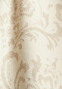 Beige tyg med ett subtilt blommönster och en texturerad yta, vilket skapar en delikat kontrast mot en krämvit bakgrund.