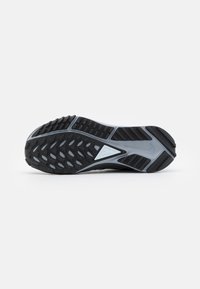 Semelle d'une chaussure de sport noire et grise avec une semelle texturée et un petit détail triangulaire au centre.