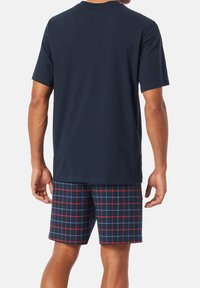 Tricou din bumbac de culoare bleumarin, asociat cu pantaloni scurți în carouri cu linii albastre și roșii pe un fundal închis. Îmbrăcăminte casual confortabilă pentru relaxare.