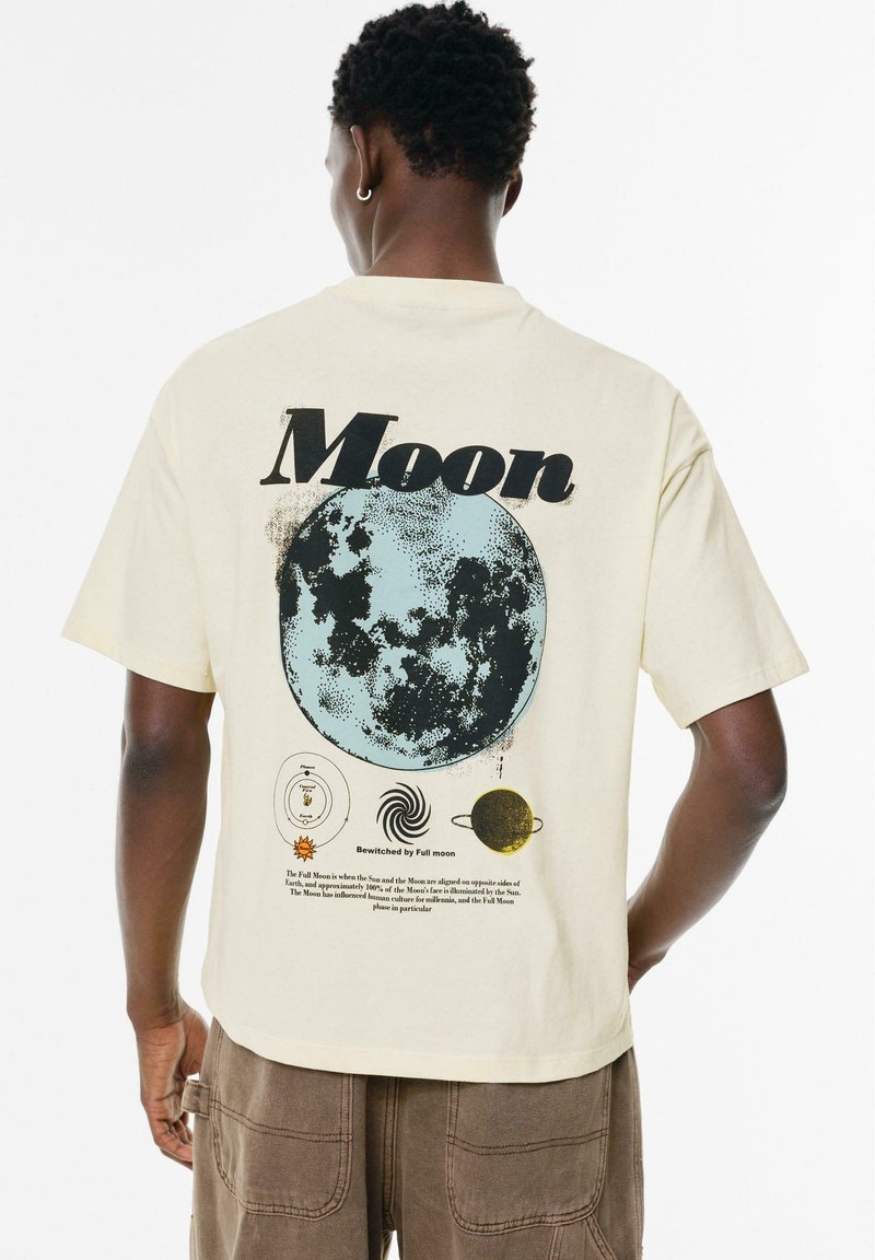 Kurze Ärmel, cremefarbenes T-Shirt mit einem blauen Mondmotiv, astronomischen Symbolen und schwarzem sowie braunem Text auf der Rückseite.