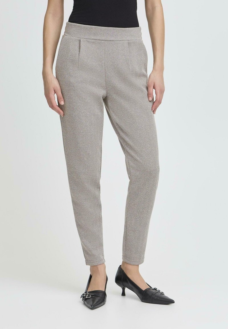 Pantalon gris slim fit à motif chevrons porté avec des chaussures noires à bout pointu et talons bas, et un haut noir, montré de la taille aux pieds.
