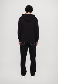 Black hoodie with a spacious hood, paired with black pants featuring decorative back pockets. The outfit is relaxed-fit and casual.