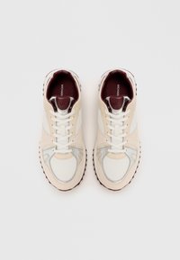 Sleek white and beige sneakers with silver accents, rounded toe, cushioned tongue, and textured rubber outsole. Branding on the interior.