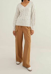 Un pull en tricot gris clair avec un col en V, associé à un pantalon cargo beige ample avec des poches avant et une taille à cordon.