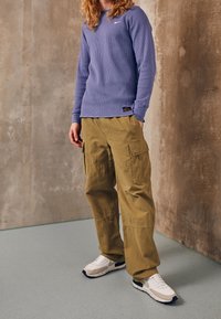 Ljuslila långärmad ribbad tröja, olivgröna cargo-byxor med sidofickor, vita och marinblå sneakers. Enkla, funktionella designelement.