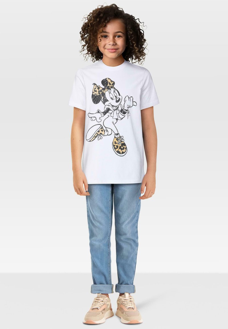 Hvit bomulls t-skjorte med et tegneseriefigurdesign som har en leopardmønster sløyfe og sko, kombinert med lys blå rullejeans og beige sneakers.