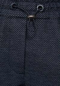 Marineblauwe stof met patroon heeft een geometrisch ontwerp, een trekkoordsluiting en metalen accenten. De textuur is glad met een lichte rek.