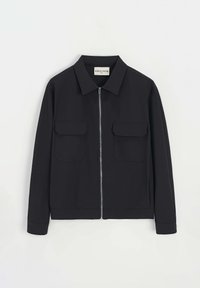 Veste noire avec une fermeture éclair à l'avant, deux poches poitrine, un col et des manches longues. Fabriquée dans un tissu lisse et texturé.
