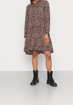 Robe à manches longues, longueur genou, avec un motif abstrait rose et noir, portée avec des bottes de combat noires à lacets sur un fond uni.