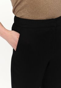 Czarne spodnie o dopasowanym kroju, z boczną kieszenią i gładką teksturą. Pas jest usztywniony, o prostym designie.