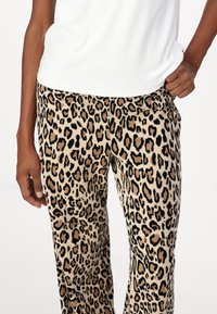 Leopard print trousers feature a soft, textured fabric with a beige base and dark brown and black spots. The fit is relaxed and casual.